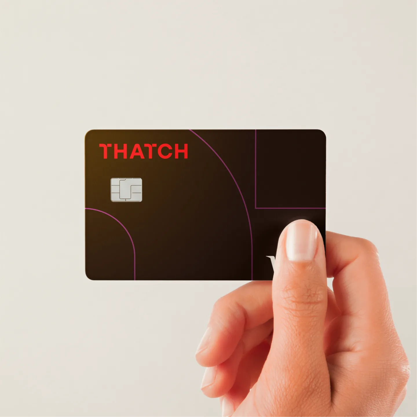 A hand holding the dark brown Thatch card, with the red wordmark and thin magenta pathway lines