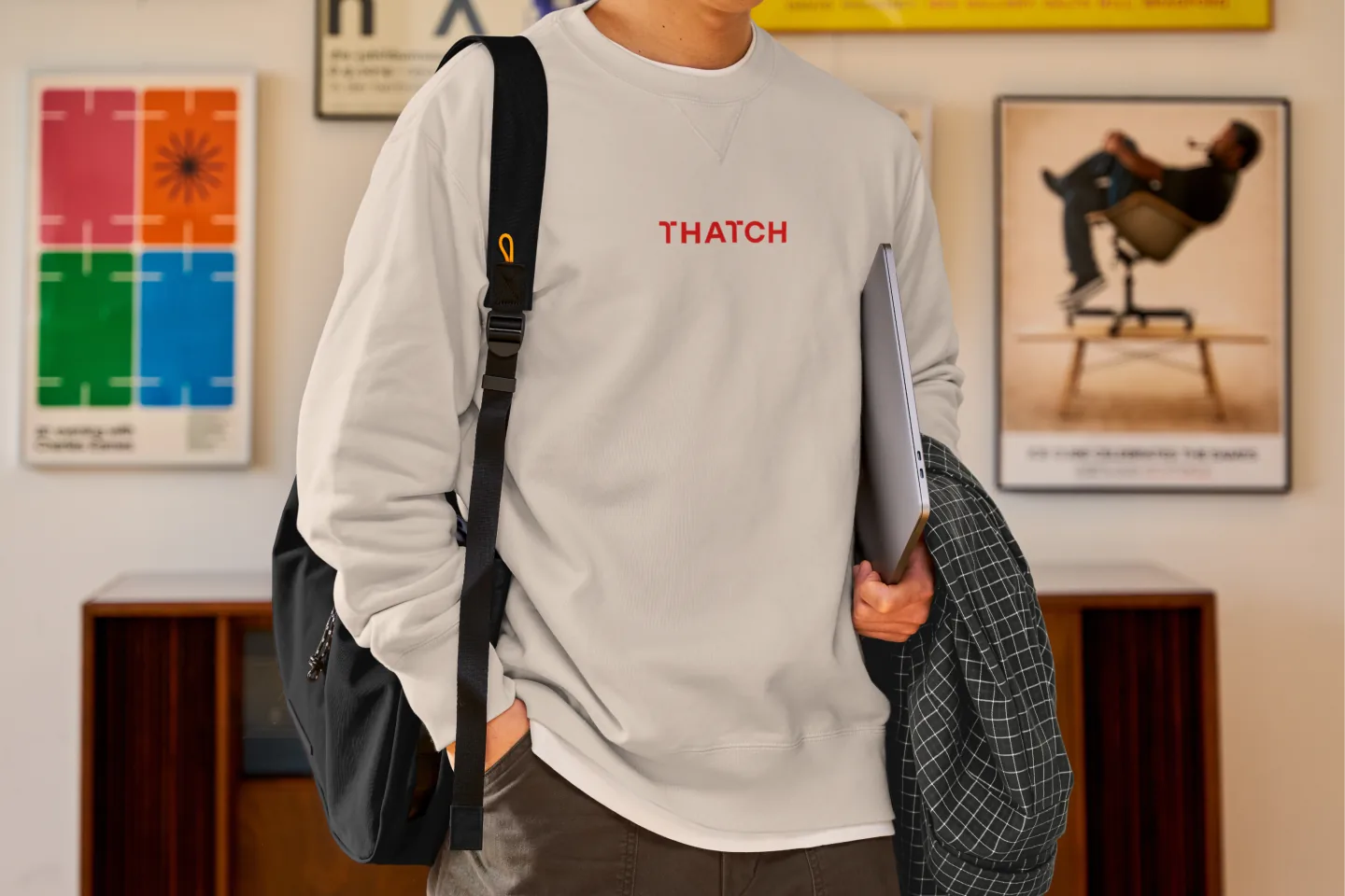 Someone wearing a cream crewneck with the Thatch wordmark embroidered in red