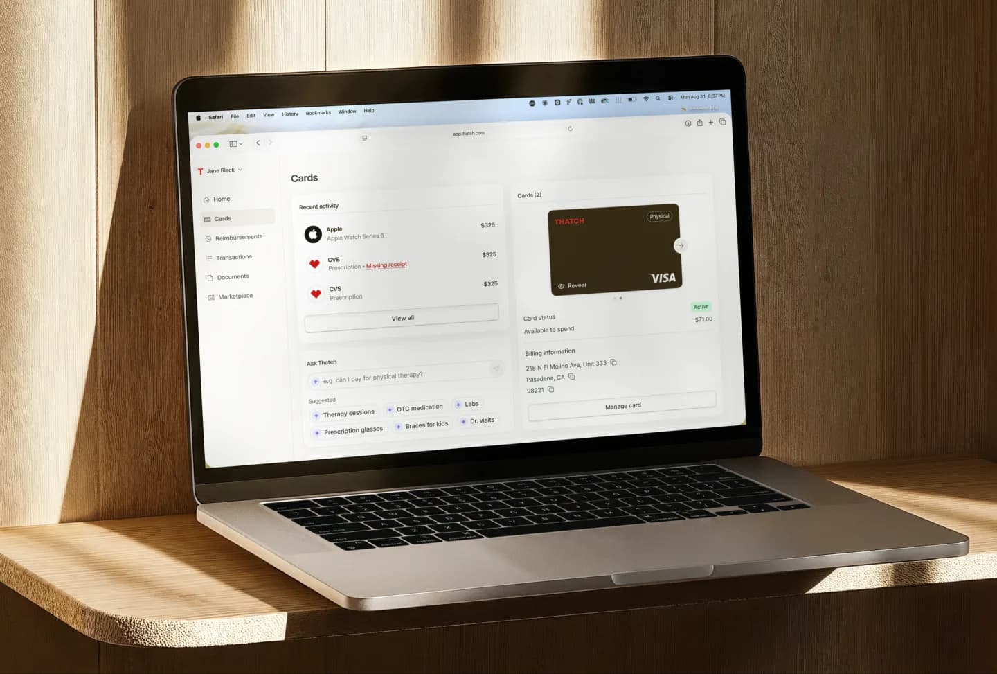 A laptop on a wood shelf showing the Thatch Cards page with recent activity, a virtual card, and Ask Thatch