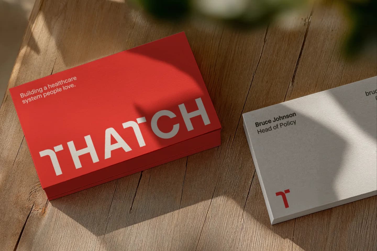A stack of red Thatch business cards reading "Building a healthcare system people love" beside a cream card with the T mark
